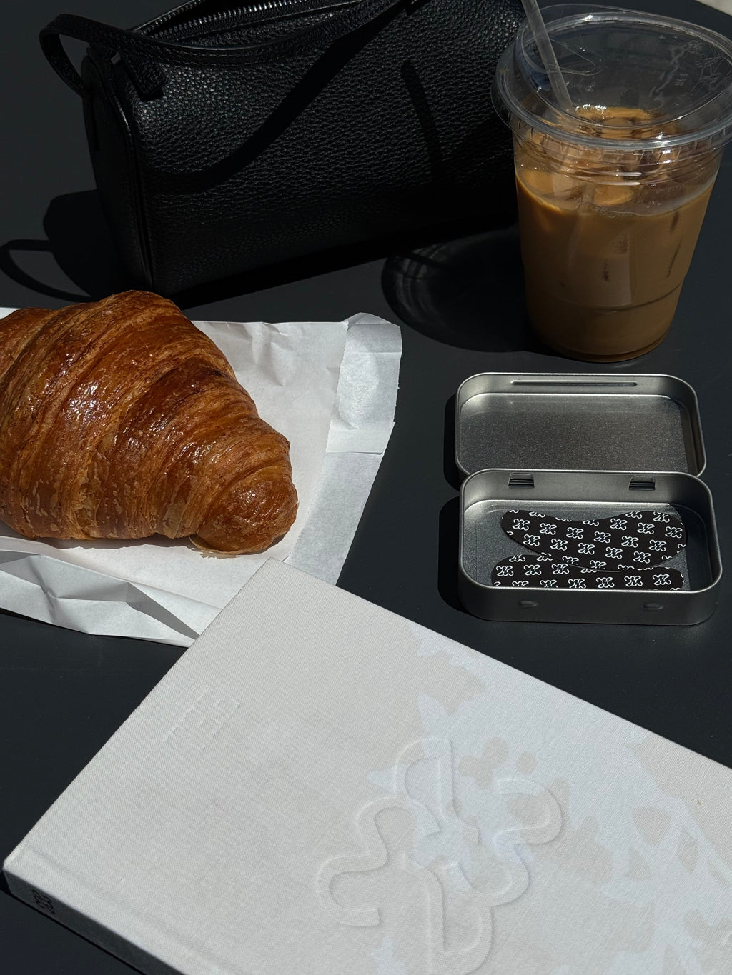 Croissant, coffee, and phone case on a black surface with a white napkin.
