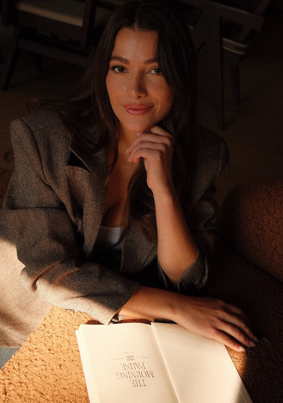 Woman sitting on a cozy couch with The Morning Pause gratitude journal open in her lap.